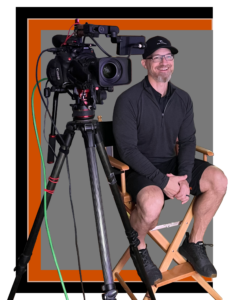 Smiling Man sitting in directors chair with camera to his right side